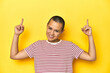 © Asier - Shaved head woman in red striped tee, yellow backdrop indicates with both fore fingers up showing a blank space.