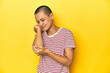 © Asier - Shaved head woman in red striped tee, yellow backdrop massaging elbow, suffering after a bad movement.