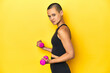© Asier - Shaved-head sportswoman lifting weights, yellow studio backdrop