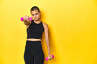 © Asier - Shaved-head sportswoman lifting weights, yellow studio backdrop