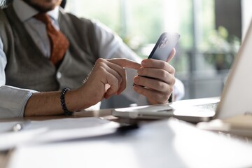 Closeup view of male hands touching mobile phone. Middle-aged man using smartphone while sitting at his desk in office