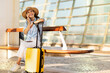 © Prostock-studio - Cheerful young european woman in hat with suitcase, call by smartphone, enjoy trip at airport, station, wait transport