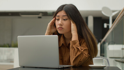 Exhausted overworked Asian chinese japanese woman student girl studying online with laptop in cafe tired sick businesswoman think difficult decision thought suffer headache massage temples pain head