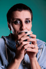 Wall Mural - Happy cheerful woman holding cup of coffee enjoying hot beverage in front of camera, having work break in studio with isolated background. Model relaxing while drinking cappucino