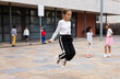 Cheerful sporty tween girl jumping rope in school yard during recess in warm autumn day