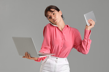 Beautiful businesswoman with devices talking by mobile phone on grey background