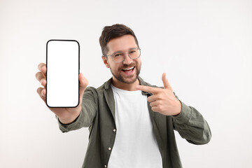 Wall Mural - Handsome man showing smartphone in hand and pointing at it on white background