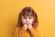 Generative AI : Happy excited little girl with pigtails wearing casual purple dress touching cheeks and looking at camera against yellow background