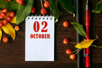 calendar date on wooden dark desktop background with autumn leaves and small apples.  October 2 is the second  day of the month