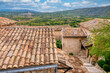 In historic Lacoste in Provence, France, traditional old stone houses with tiled roofs overlook the lush French countryside, with the village of Bonnieux visible in the distance.