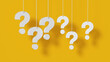 © ImagesRouges - Many question marks white hanging on yellow wall background.