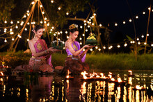 Two Thai Woman Holding A Krathong Sitting On A Raft By The River, Asian Women In Traditional Thai Costumes Bring Krathongs To Float On Loi Krathong Day, Traditions And Culture Of Thailand,