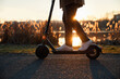 © baranq - Man riding electric scooter in city park during autumn sunset