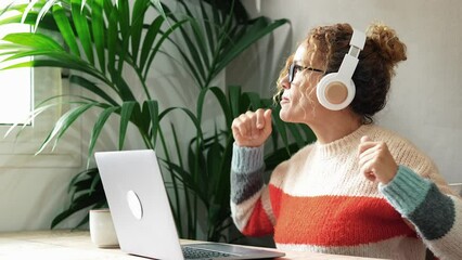 Wall Mural - Happy adult youth woman at home dancing and listening music with headphones and laptop connection. Modern smart people female at work in indoor house leisure activity dance and enjoy tie alone