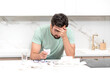 © Vitaliy - Close up of unhappy man sitting at the table, stressed and confused by calculate expense from invoice or bills, have no money to pay mortgage or loan. High prices and spending money concept