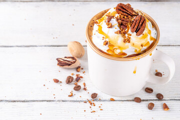 Autumn winter hot spicy drink, Maple Pecan coffee latte with whipped cream cup on white wooden table with cozy sweater and ingredients copy space