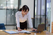 © amnaj - Smiling young happy Asian businesswoman working with laptop and documents in office. Accountant or beautiful asian female worker working happily in the office...