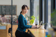 © amnaj - Young Asian Woman Working on Laptop in a Cozy Cafe, Freelancer at a Coffee Shop