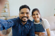 © itchaznong - Indian couple taking selfie photo or video call while sitting on the couch at home