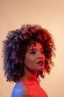Biracial woman with curly hair wearing pink eyeshadow and lipstick in red and blue light, copy space