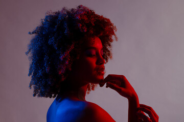 Wall Mural - Biracial woman with curly hair touching chin in blue and red light