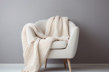 A white armchair with a white woolen blanket on it. The concept of winter minimalism.