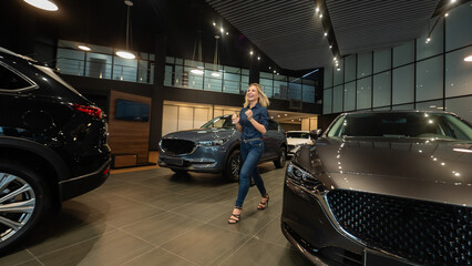  Young caucasian woman rejoices buying a car in a car dealership. 