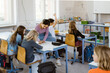 © Maskot - Female teacher assisting schoolgirls while sitting on desk in classroom
