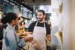 © Maskot - Smiling mature salesman discussing over product with female customer at delicatessen
