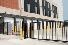 Line Row Of Exterior Outdoors Outside Building Public Storage White Garage Units Behind Black Metal Fence Mechanical Gate On Cement Pavement