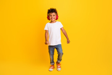 Wall Mural - Full length photo of funky cheerful little boy dressed white t-shirt walking enjoying songs earphones isolated yellow color background