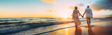 Fototapeta  - Senior couple walking along a beach in the sunset. Concept of retirement, mature love and travel. Shallow field of view with copy space.