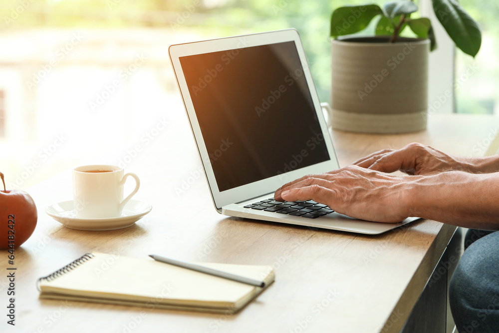 Mature man with laptop messaging in kitchen, closeup