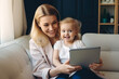 © mila103 - happy mother and daughter looking at digital tablet at home in living room