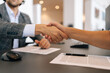 © dikushin - Close-up hands of unrecognizable business people handshaking after negotiation for business deal and acquisition in office sitting at desk. Closeup of businessmen sign contract agreement on paper.