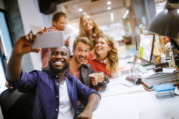 Wall Mural - Diverse group of coworkers taking a selfie on a smartphone in the office of a startup company