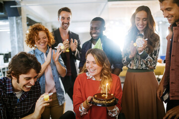 Young and diverse group of people celebrating a surprise birthday party in the office of a startup company