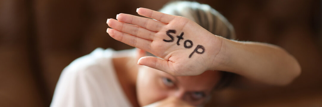 Scared woman covering face with palm with stop inscription