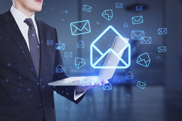 businessman hands using laptop with glowing email letter icons on blurry office interior background.