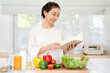 © Fahng - Woman reading recipe for simple summer salad in cookbook. Simple healthy food concept