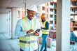 © Dragana Gordic - Businessman using his smartphone while on a construction site. Portrait of young engineer in vest with white helmet standing on construction site, smiling and holding smartphone for worker