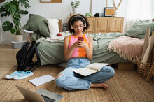Teenage girl wearing wireless headphones using mobile phone on rug at home
