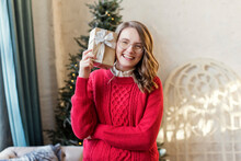 Happy Woman Wearing Red Sweater Holding Christmas Gift At Home