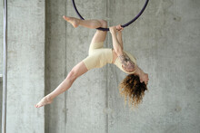 Woman practicing gymnastics on aerial hoop in front of concrete wall