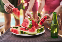 Hands Of Friends Holding Slices Of Watermelon At Table