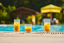 Glasses Of Orange Juice With Swimming Pool In Background At Resort