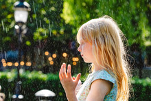 Blond Girl Enjoying Fountain Water Falling In Park