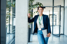 Smiling Businesswoman Leaning On Column In Corridor