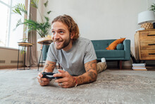 Happy Man Lying On Carpet And Playing Video Game At Home