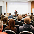 © kasto - Speaker giving a talk in conference hall at business event. Rear view of unrecognizable people in audience at the conference hall. Business and entrepreneurship concept